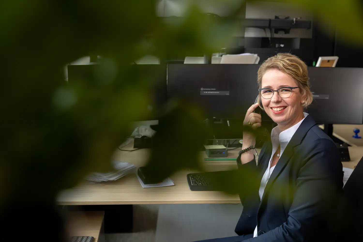 GKS-medewerkster achter bureau kijkt lachend richting camera.