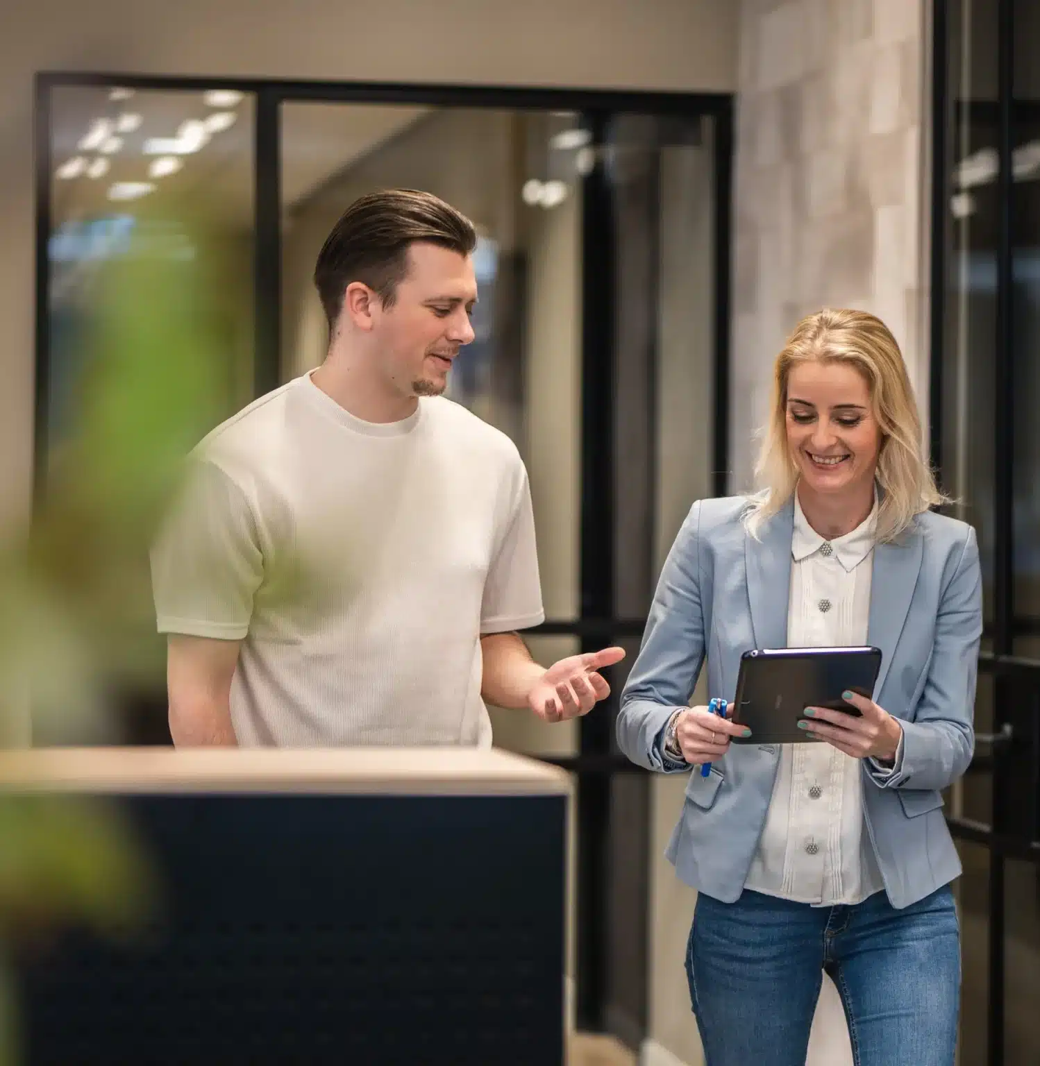 Twee collega's van GKS overleggen met tablet in moderne kantooromgeving.